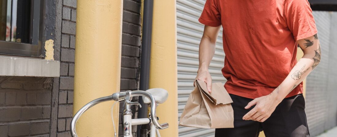 US bike food delivery driver in red shirt with takeout paper bag and insulated delivery backpack