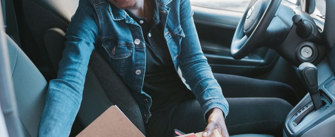 Smiling pizza delivery driver picking up pizza boxes from her delivery van