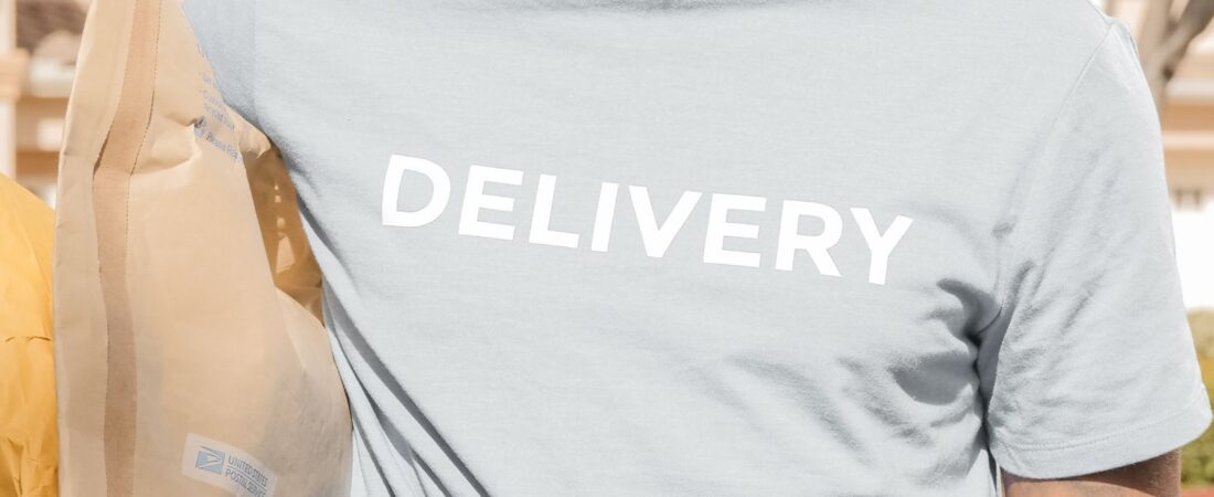 Smiling US delivery driver in DELIVERY shirt carrying packages to a customer